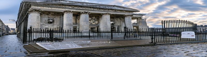 Panoramic view of the Bank of England's neoclassical facade on Threadneedle Street in early morning light, grey limestone columns and iron gates, ornate clock face visible, wet cobblestones reflecting the sky, scattered printed financial stability report on a wrought-iron bench in the foreground, no people no faces no hands