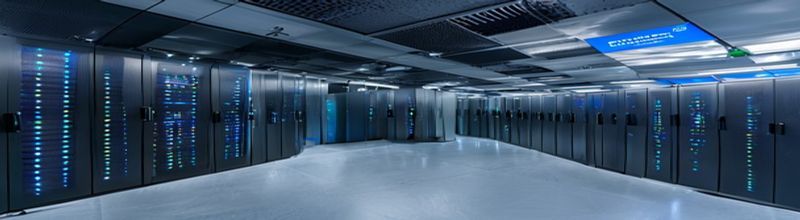 Panoramic view of an empty hospital corridor at night, polished pale floor reflecting recessed ceiling lights, a row of softly glowing computer terminals on counters along one wall, no people no faces no hands