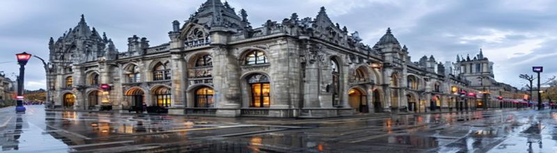 Panoramic view of the Royal Courts of Justice in London on a grey afternoon, ornate Victorian Gothic stone facade with high pointed arches and spires, wet pavement reflecting the building, traffic lights changing in the foreground, no people no faces no hands